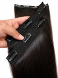 A hand holding a bundle of long, straight black hair clip-in extensions against a plain white background.