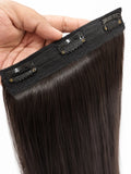 A close-up of a hand holding a straight, dark brown hair clip-in extension piece against a white background, showing the black adhesive band and multiple clip attachments.
