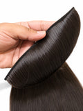 A close-up of a hand holding a dark brown, straight hair extension piece against a white background.