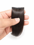 A hand holding a straight, dark brown hair extension piece against a plain white background.